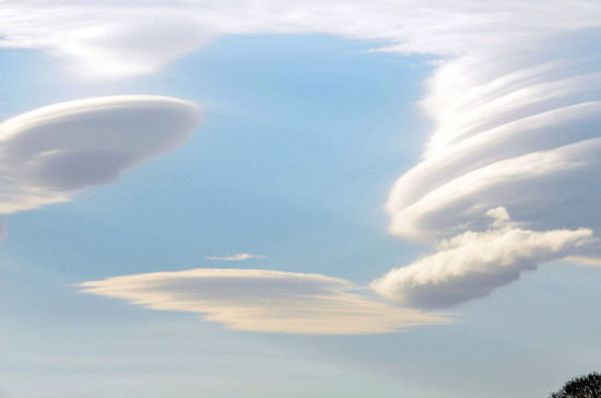 照片中的碟状云犹如茶碟或透镜一样高悬在空中，有的单独悬挂，有的三四个叠加在一起。